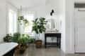Bathroom with potted plants, round mirror above black vanity, and hanging planters by large windows.