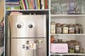 Stainless steel fridge with googly eyes, books on top, and pantry shelves with jars and a pink Smeg toaster.