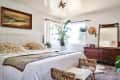 Cozy bedroom with a large bed, wooden dresser, plants, and a seascape painting above the headboard.