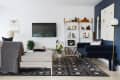 Modern living room with a navy sofa, wall-mounted TV, patterned rug, and white shelving with books and decor.