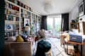 Cozy reading room with bookshelves, beige armchairs, a patterned rug, and large windows overlooking a garden.