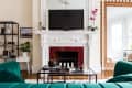 Living room with green velvet sofas, ornate white fireplace, large mirror, and a black TV above the mantel.