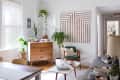 Mid-century modern living room with wooden dresser, green chair, geometric wall art, and various potted plants.