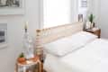 Bedroom with a woven headboard, white bedding, side table with a statue lamp, and framed art on the walls.