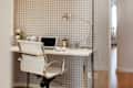 Home office with a white desk, laptop, desk lamp, and a white chair against a houndstooth-patterned wall.