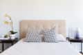 Beige tufted headboard with patterned pillows, flanked by side tables with a plant and a lamp.