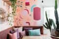 Colorful abstract mural in a cozy corner with a brown bench, assorted pillows, hanging plants, and a large cactus.
