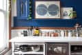 Kitchen with blue wall, white counter, small fridge, spice jars, cookware, and framed art.