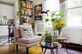 Living room with pink chair, face pillow, cat on perch, sunflowers in vase, and bookshelves near kitchen.