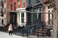 Row of colorful brownstone houses with ornate iron railings, two people walking on the sidewalk.
