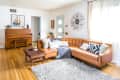 Mid-century living room with a brown leather sectional, wooden piano, geometric pillows, and a sunburst wall clock.