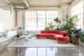 Loft living room with red sectional sofa, large windows, numerous potted plants, and a cat on the sofa.