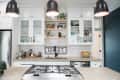 Modern kitchen with white cabinets, glass doors, black faucet, and pendant lights. Basket of fruit on the counter.