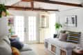 Cozy living room with white French doors, striped pillows on a daybed, and plants on shelves.