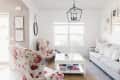 Living room with floral armchairs, gray sofa, white coffee table, books, and geometric chandelier under a large window.
