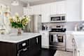 Modern kitchen featuring a marble-topped island, dark cabinetry, stainless steel appliances, and a floral centerpiece.