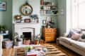 Living room with mint green walls, a white fireplace, wooden chest, bookshelves, and a beige sofa with patterned cushions.