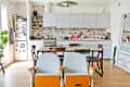 Eclectic kitchen with brick backsplash, wooden table, mismatched chairs, and a fridge covered in magnets.