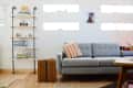 Gray sofa with orange patterned pillow, wooden side table, and wall-mounted shelves filled with books and decor items.