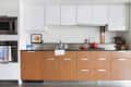 Modern kitchen with wooden cabinets, white upper cupboards, red kettle, and a cat on the counter.