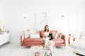 Woman sitting on a pink sofa with a black dog in a bright, modern living room with white decor and gold accents.