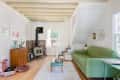 Cozy living room with green sofa, wood stove, record player, and mid-century decor. White rug and wooden floors.