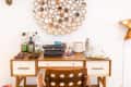 Mid-century desk with a typewriter, liquor bottles, sunglasses, and a circular mirror wall decor.