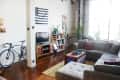 Loft living room with gray sectional sofa, colorful cushions, bicycle, TV, bookshelves, and large windows.