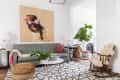 Living room with gray sofa, large floral artwork, geometric rug, wicker ottoman, and green plant near a fireplace.