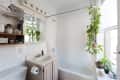 Bathroom with white tiles, hanging plants, a sink, and a bathtub. Shelves hold towels and toiletries.