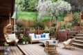 Outdoor patio with wooden deck, wicker furniture, hanging chair, potted plants, and a blooming tree.