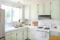 Mint green kitchen cabinets, white countertops, gas stove, and potted plants by a large window.