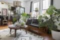 Living room with large windows, plants, a wooden coffee table, and a black sofa with patterned cushions.
