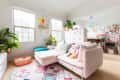 Bright living room with a pink sofa, colorful cushions, plants, and a geometric rug. A small dog sleeps on the sofa.