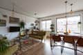 Mid-century modern living room with green sofa, glass coffee table, dining area, and large windows with plants.