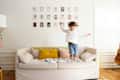 Child jumping on a beige sofa with colorful pillows, wall art above, and a guitar in the corner.