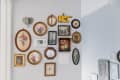 Eclectic gallery wall with vintage floral art, a yellow pointing hand, and an elephant head above a thermostat.
