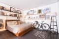 Bedroom with a wooden bed, gray bedding, wall art, bookshelves, and a bicycle against the wall.