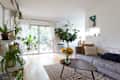 Bright living room with gray sofa, wooden coffee table, sunflowers, and large plants near sliding glass doors.