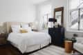 Cozy bedroom with a beige headboard, white bedding, yellow accent pillow, black cabinet, and large mirror.