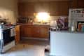 Cluttered kitchen with wooden cabinets, stove, fridge, and countertop filled with dishes and appliances.