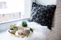 Cozy real home decoration, burning candles on golden tray with pillow on white faux fur on windowsill