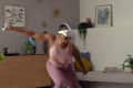 Person in pink activewear playing VR game in a living room with plants, art, and a wooden cabinet.