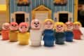 Toy figurines with various expressions in front of a blue and yellow dollhouse.