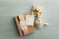 Wedding gifts with gold ribbons, a wish list card, and white roses on a light blue surface.