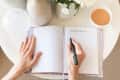 Hands writing in gratitude journal with cup of coffee on table