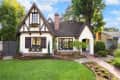 Tudor-style house with steep gable roof, brick chimney, and manicured garden with a stone path.