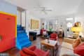 Colorful living room featuring red chairs, a wooden table, blue stairs, and large windows with plants.
