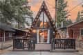 A-frame cabin with string lights, wooden deck, and large windows, surrounded by trees at sunset.