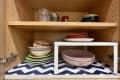 Kitchen cabinet with dishes, glasses and zigzag blue and white contact paper. White IKEA variera shelf with small plates on top